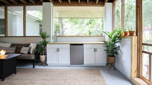 A modern kitchen with white cabinets, a built-in dishwasher, and a large window with a view of greenery. - Charleston House with Private Pickleball Court! (Charleston)