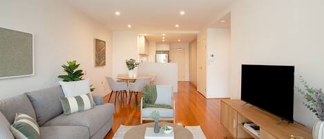 A modern living room with a grey sofa, a round coffee table, a flat-screen TV, and a dining area with a table and chairs.