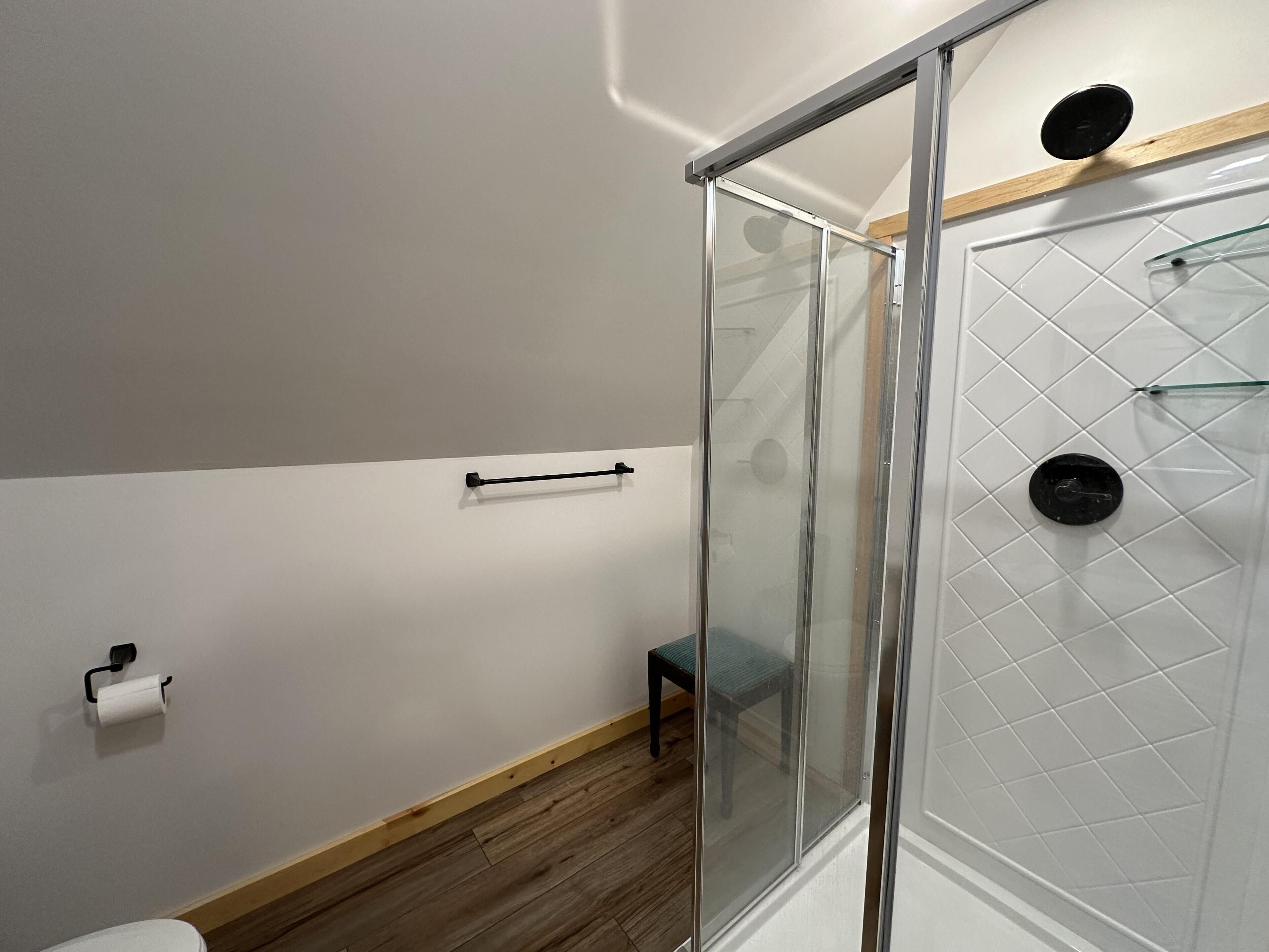 Un baño moderno con cabina de ducha de vidrio, suelo de madera y un taburete de madera.