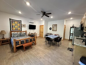Ein Schlafzimmer mit einem Bett, einem Nachttisch und einem Fernseher. Es gibt einen Essbereich mit Tisch und Stühlen.