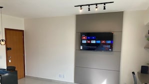 Una sala de estar moderna con un televisor de pantalla plana montado en la pared, un comedor con mesa y sillas, y una puerta con marco de madera.