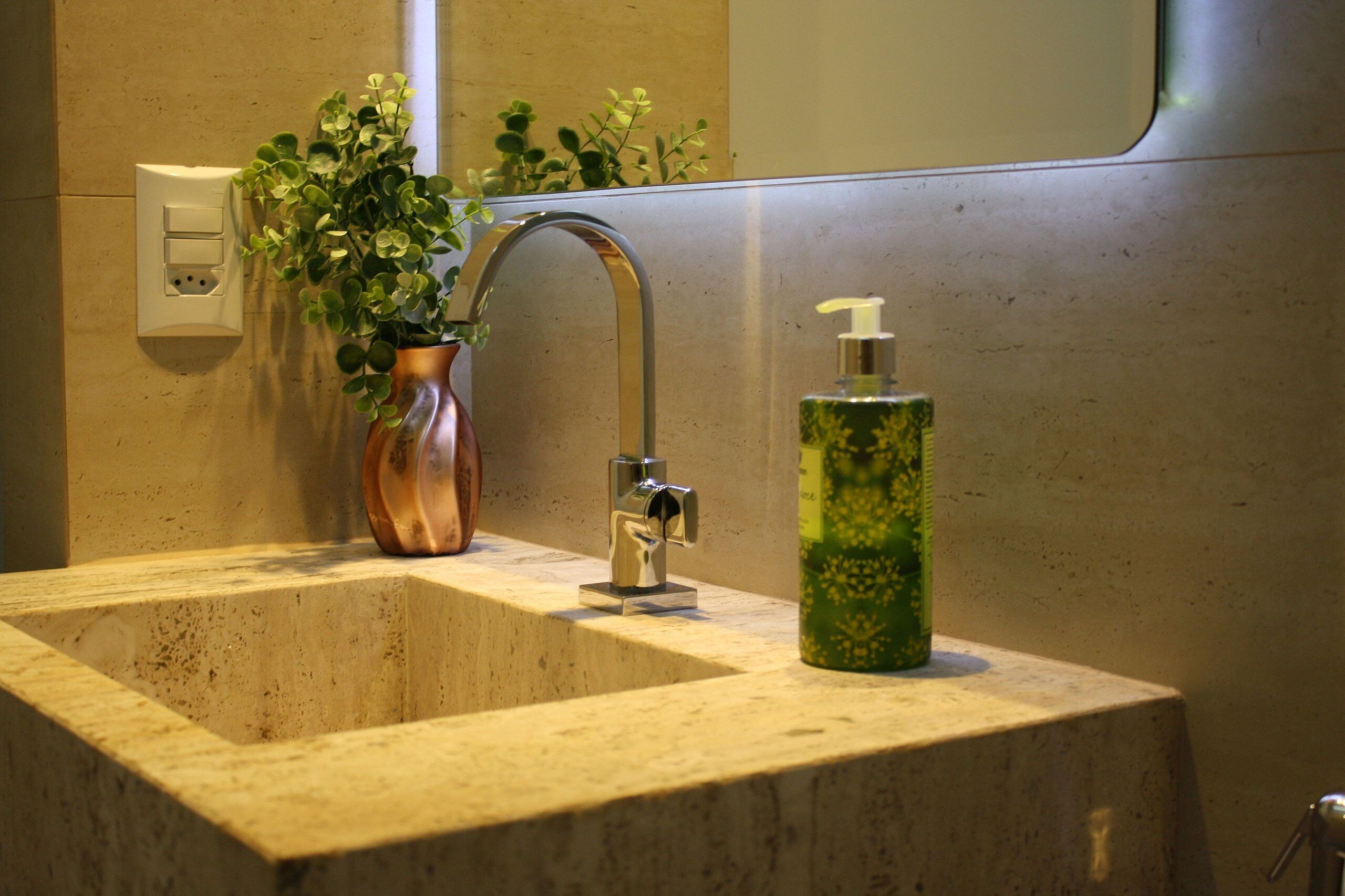 A bathroom sink with a modern faucet, a potted plant, and a soap dispenser.