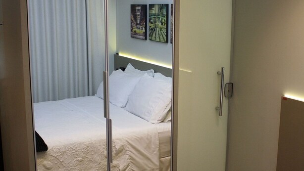 Een slaapkamer met een spiegelkast, een bed met witte lakens, een houten vloer en een airconditioner aan het plafond.