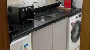 Une cuisine compacte équipée d’un four à micro-ondes, d’un petit réfrigérateur, d’un lave-linge et d’un évier.