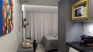A compact hotel room with a bed, a microwave, a coffee maker, and a small table with a chair. - Apartment Asa Norte CLN 110 ap 111 (Brasília)