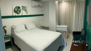 A hotel room with a bed, a desk, a chair, a small table, a plant, and a curtain. - Loft 34m² Asa Norte CLN 213 (Brasília)
