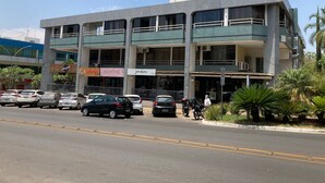 A multi-story building with commercial spaces on the ground floor, including a car dealership and a café. - Loft 34m² Asa Norte CLN 213 (Brasília)
