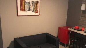 Ein kompakter Wohnbereich mit einem schwarzen Sofa, einem roten Sessel, einer Küchenzeile mit einem roten Schrank und einem gerahmten abstrakten Gemälde an der Wand.