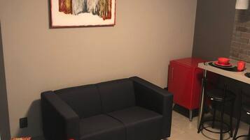 Um espaço compacto com sofá preto, poltrona vermelha, cozinha compacta com armário vermelho e uma pintura abstrata emoldurada na parede.