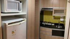 A compact kitchen with a microwave, a small refrigerator, a stove, and a sink. - Apartment Asa Sul Golden Place (Brasília)