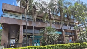 Un edificio de varios pisos con balcones, un letrero verde y una palmera frente a él.