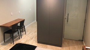 Ein Zimmer mit einem Holztisch, zwei Stühlen, einem dunklen Kleiderschrank und einer Glastür.