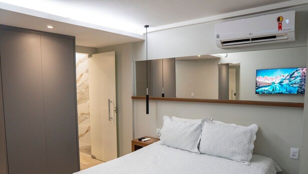 Ein Hotelzimmer mit Bett, Wandfernseher, Klimaanlage und Nachttisch aus Holz.