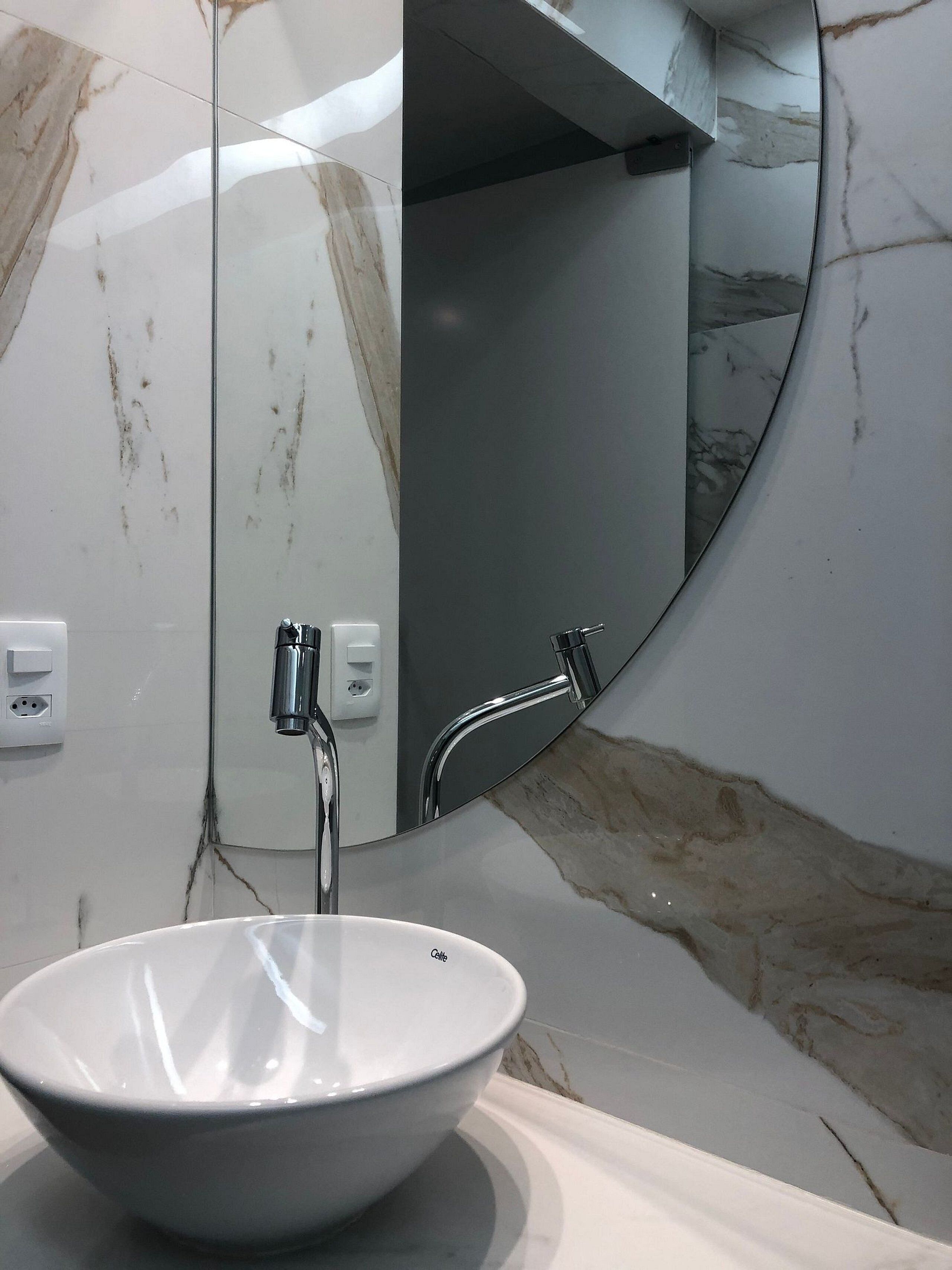 Ein Badezimmer mit einem weißen Marmorwaschbecken, einem Chrom-Wasserhahn und einem großen Spiegel.