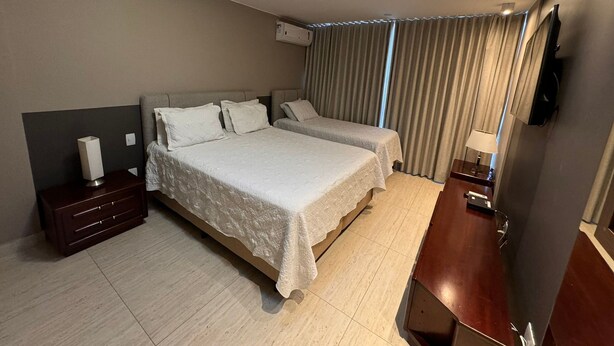 Une chambre d’hôtel moderne avec deux lits, une table de chevet, un téléviseur et un luminaire au plafond.