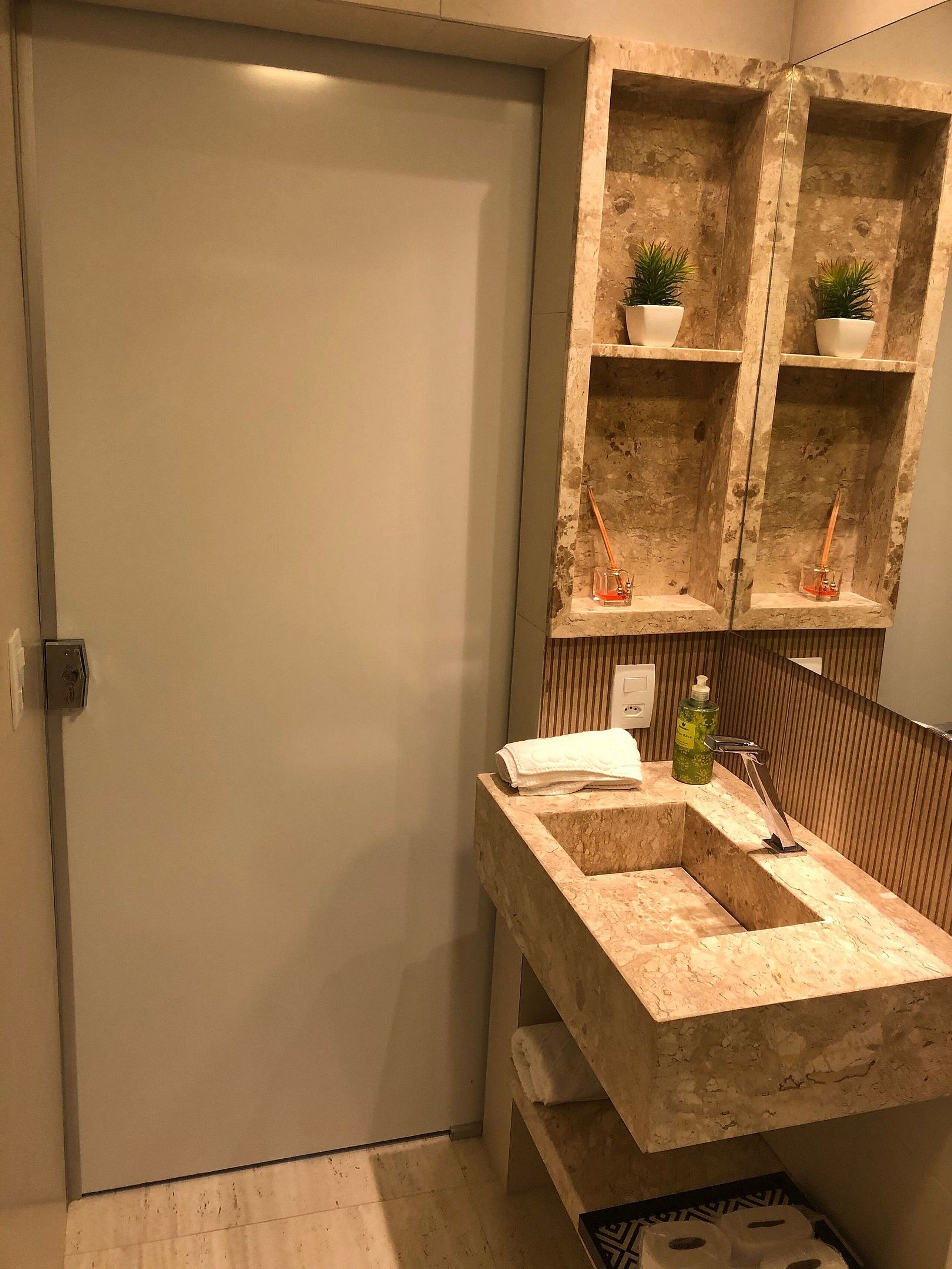 Een badkamer met een marmeren wastafel, een spiegel en planken met planten en toiletartikelen.
