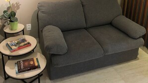 Un canapé gris, deux petites tables rondes et une plante en pot avec des fleurs jaunes.