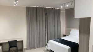 A modern hotel room with a bed, desk, chair, and curtains.
