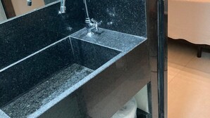 Un baño con lavamanos de granito negro, un espejo y un dispensador de toallas.