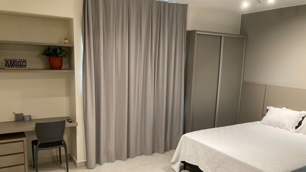 Una habitación de hotel moderna con cama, escritorio, silla y un ventanal con cortinas.