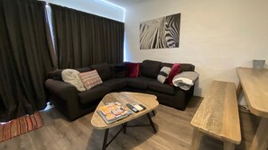A living room with a sectional sofa, a coffee table with magazines, a zebra print artwork, and a wooden bench. - Alpine Mountain View 3 - Jindabyne (Jindabyne)
