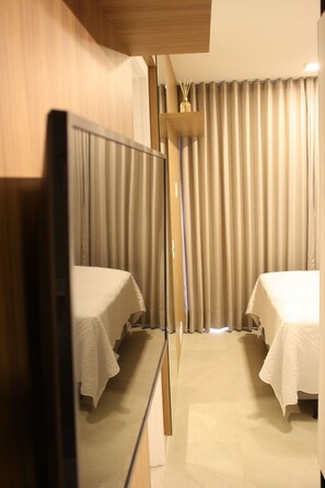 Two single beds with white linens, a large mirror, and light-colored walls.