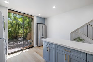 Eine moderne Küche mit einer Schiebeglastür, die zu einem Garten führt, einem eingebauten Kühlschrank und einer weißen Arbeitsplatte.