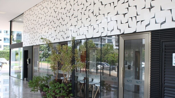 Un bâtiment moderne avec une façade à motifs, de grandes fenêtres en verre et des plantes en pot à l’extérieur.