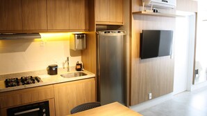 Une cuisine moderne avec des meubles en bois, un réfrigérateur en acier inoxydable, un four encastré, une cuisinière à gaz et un téléviseur fixé au mur.