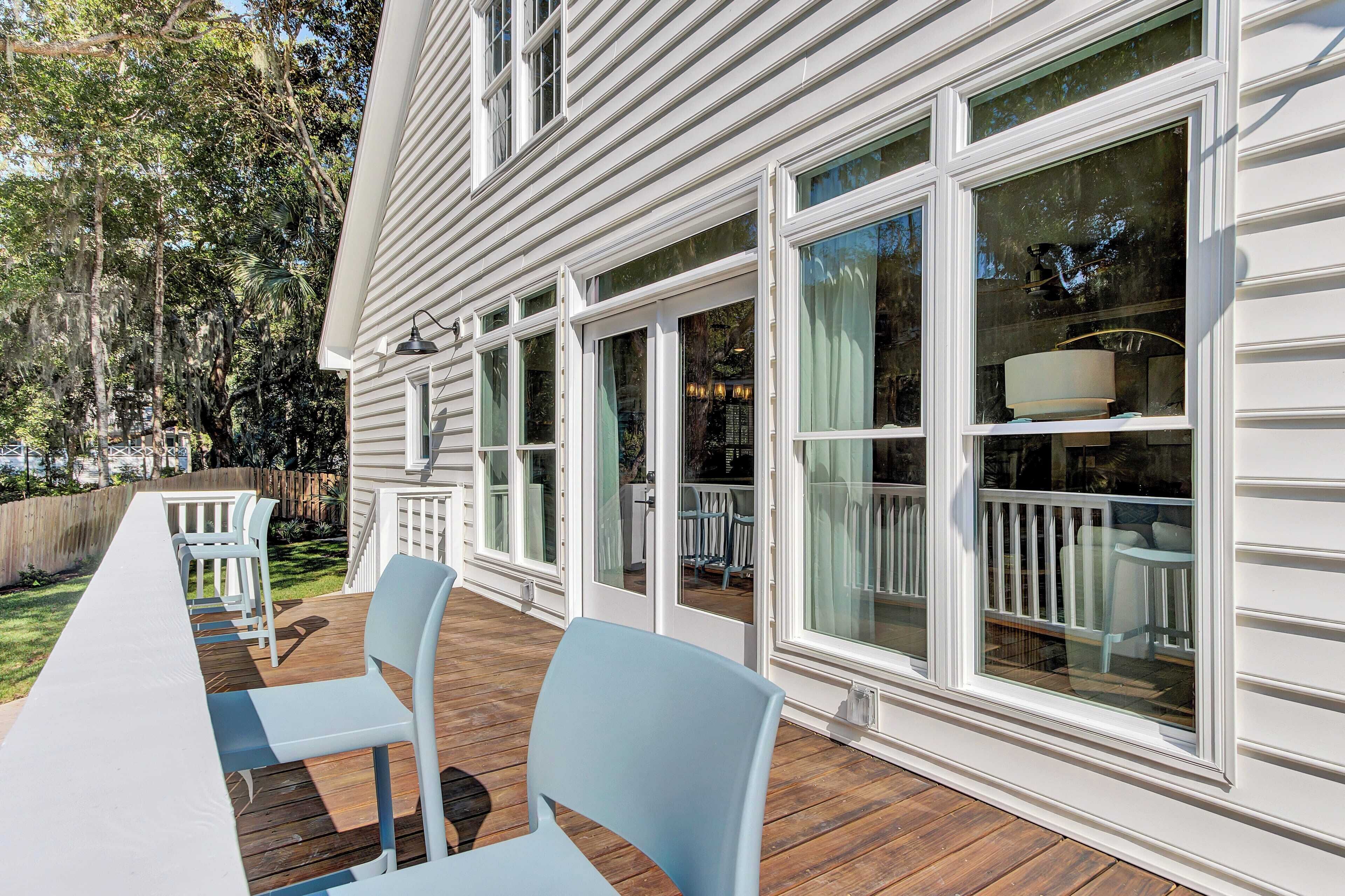 A covered patio with a long table and chairs, large windows, and a wooden deck.
