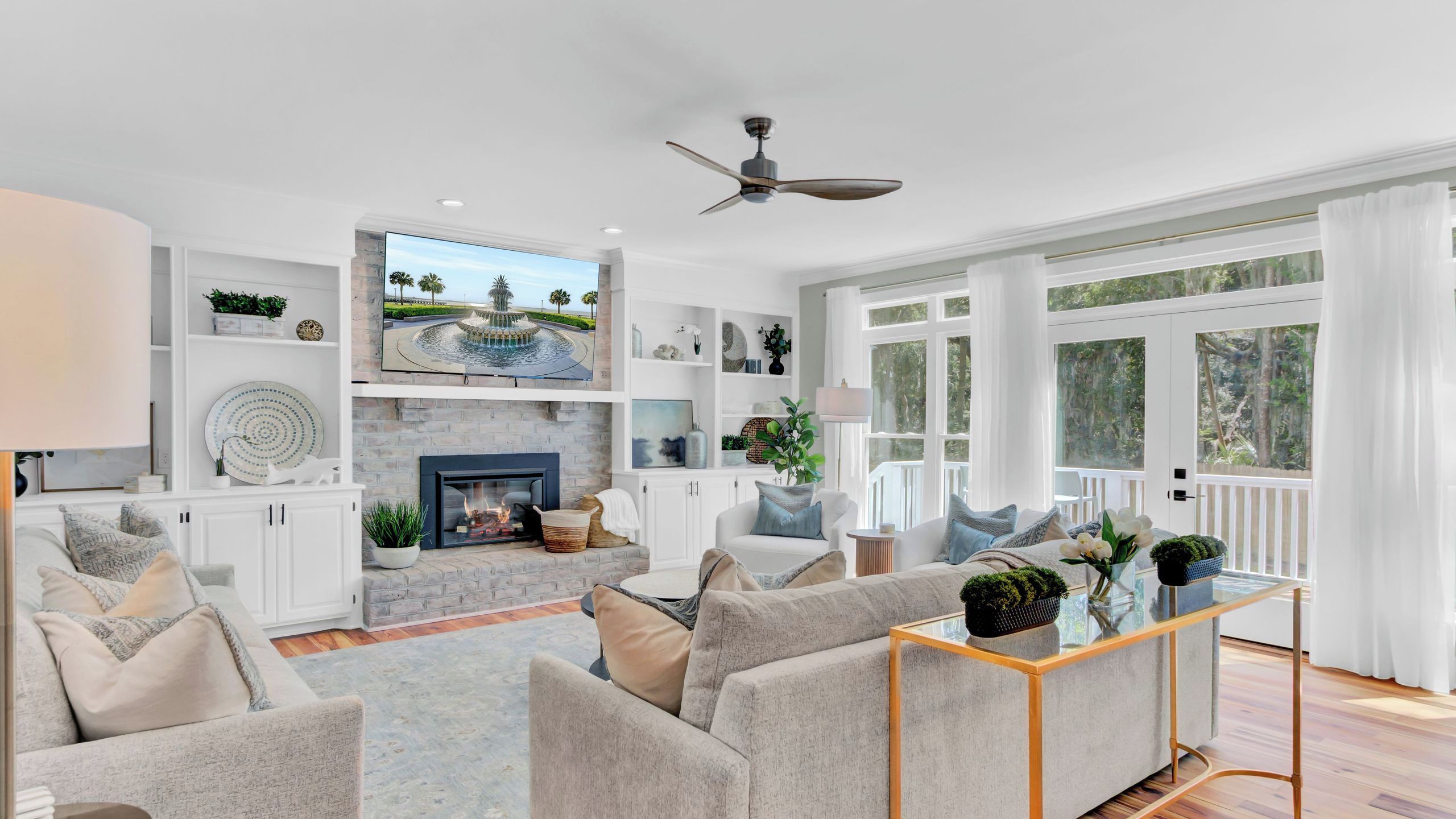 A spacious living room with a fireplace, comfortable seating, a television, and large windows.