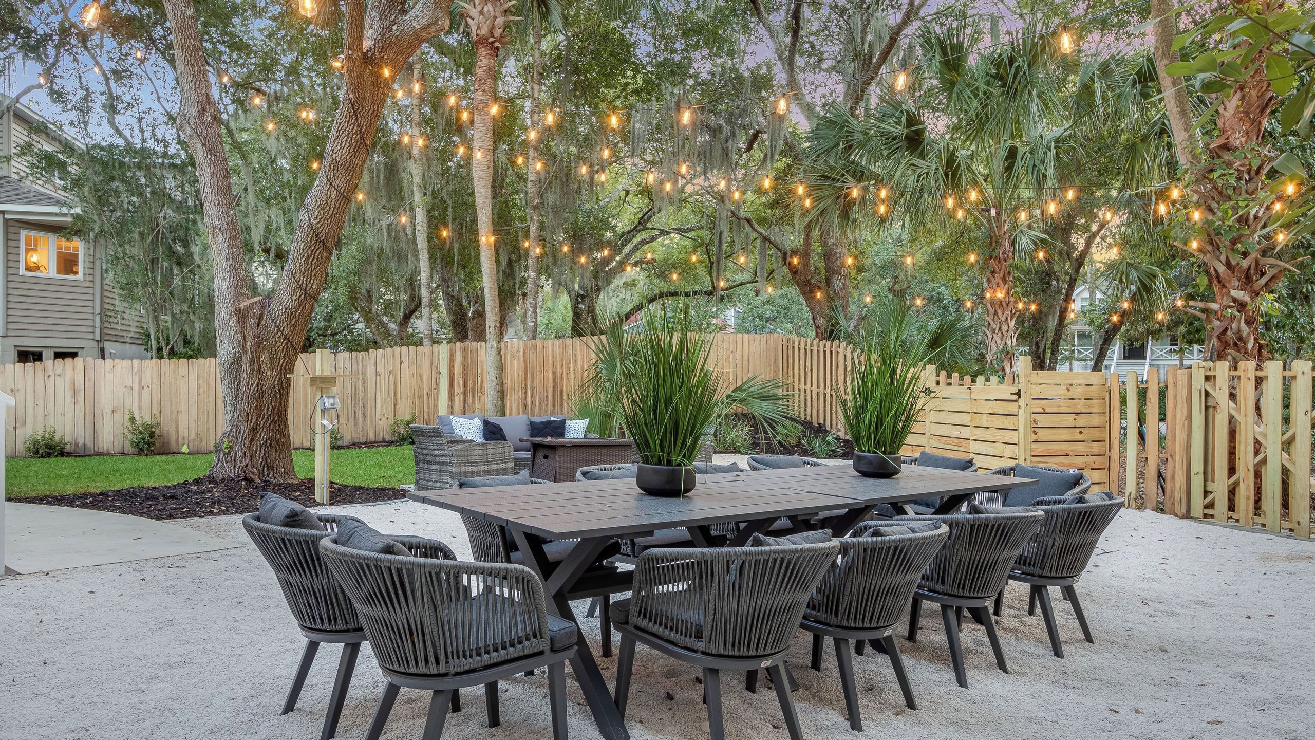 An outdoor patio with a table and chairs, surrounded by trees and string lights.