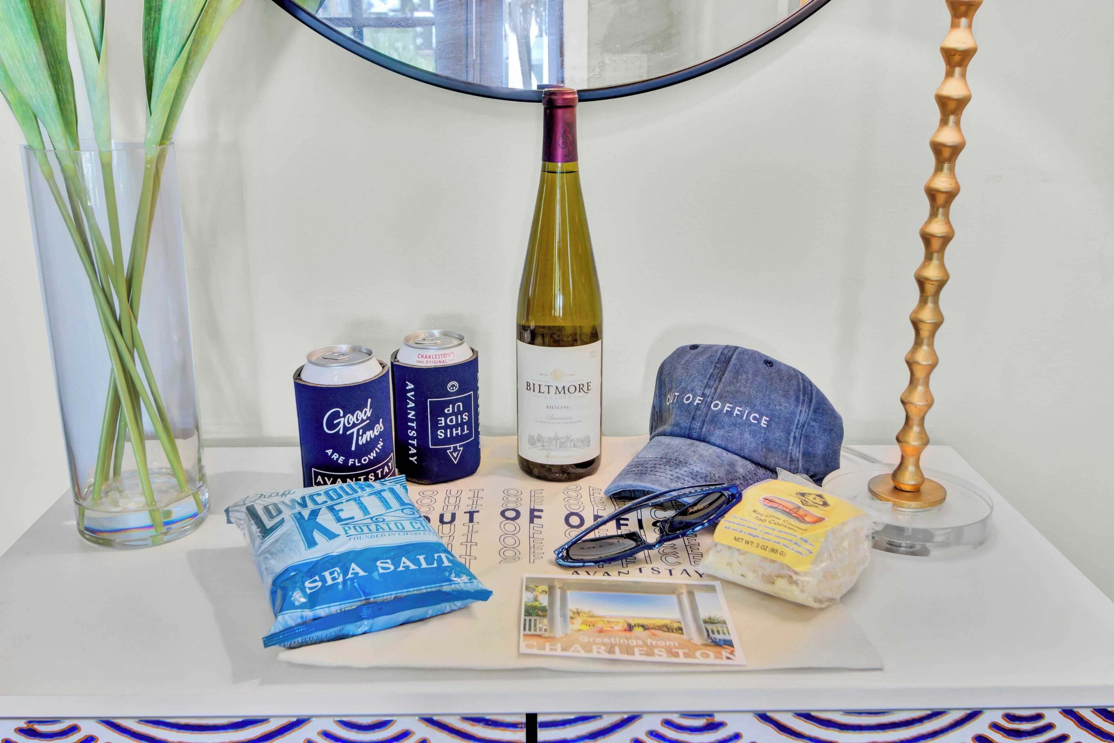 Una mesa con una botella de vino, dos latas, un paquete de sal marina, un tapón, un par de gafas y un folleto.