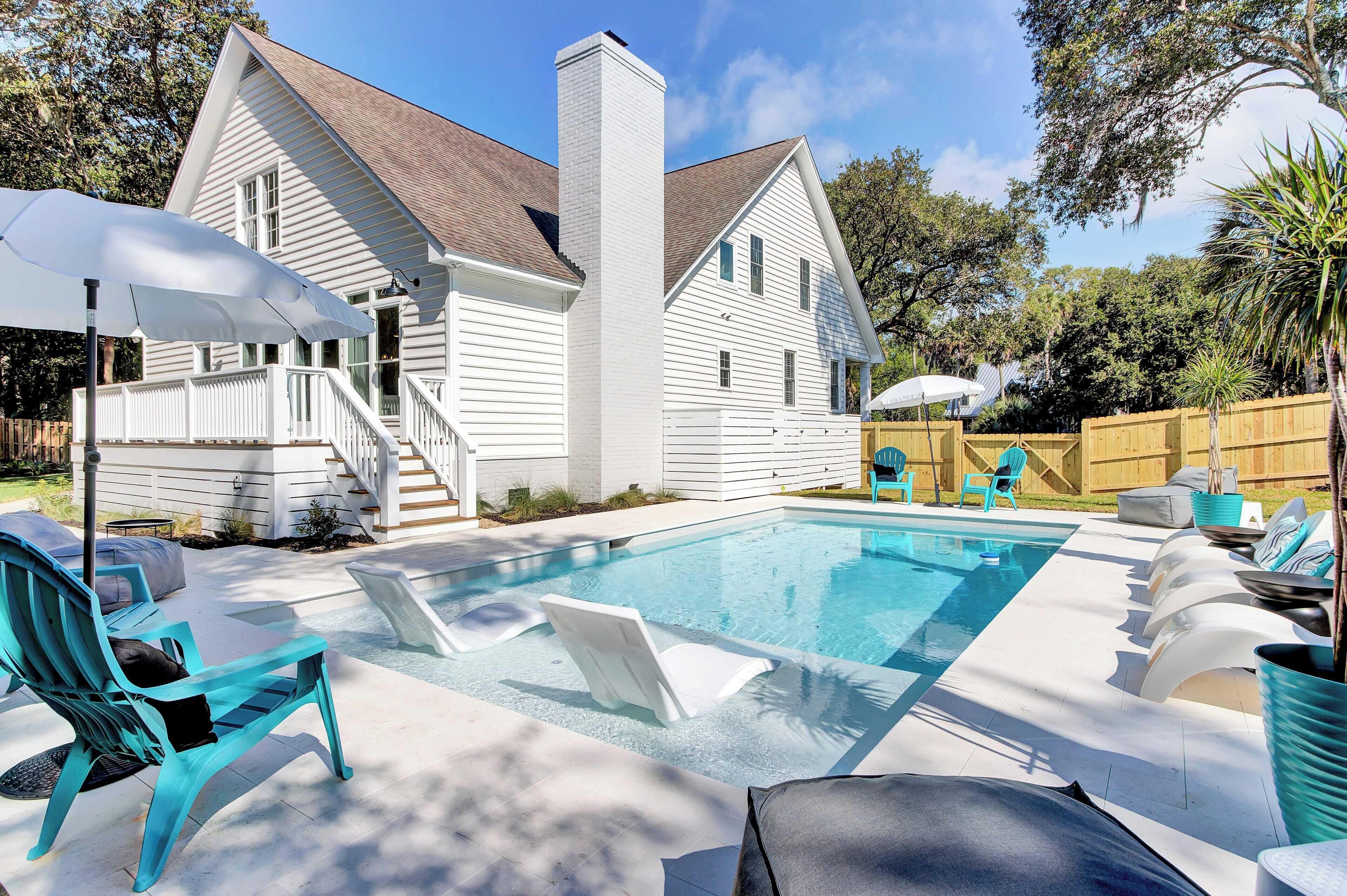 Une maison blanche avec une piscine, du mobilier d’extérieur et une terrasse en bois.