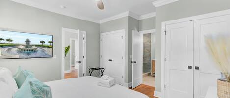A bedroom with a bed, a ceiling fan, a painting of a fountain, and white doors leading to other rooms.