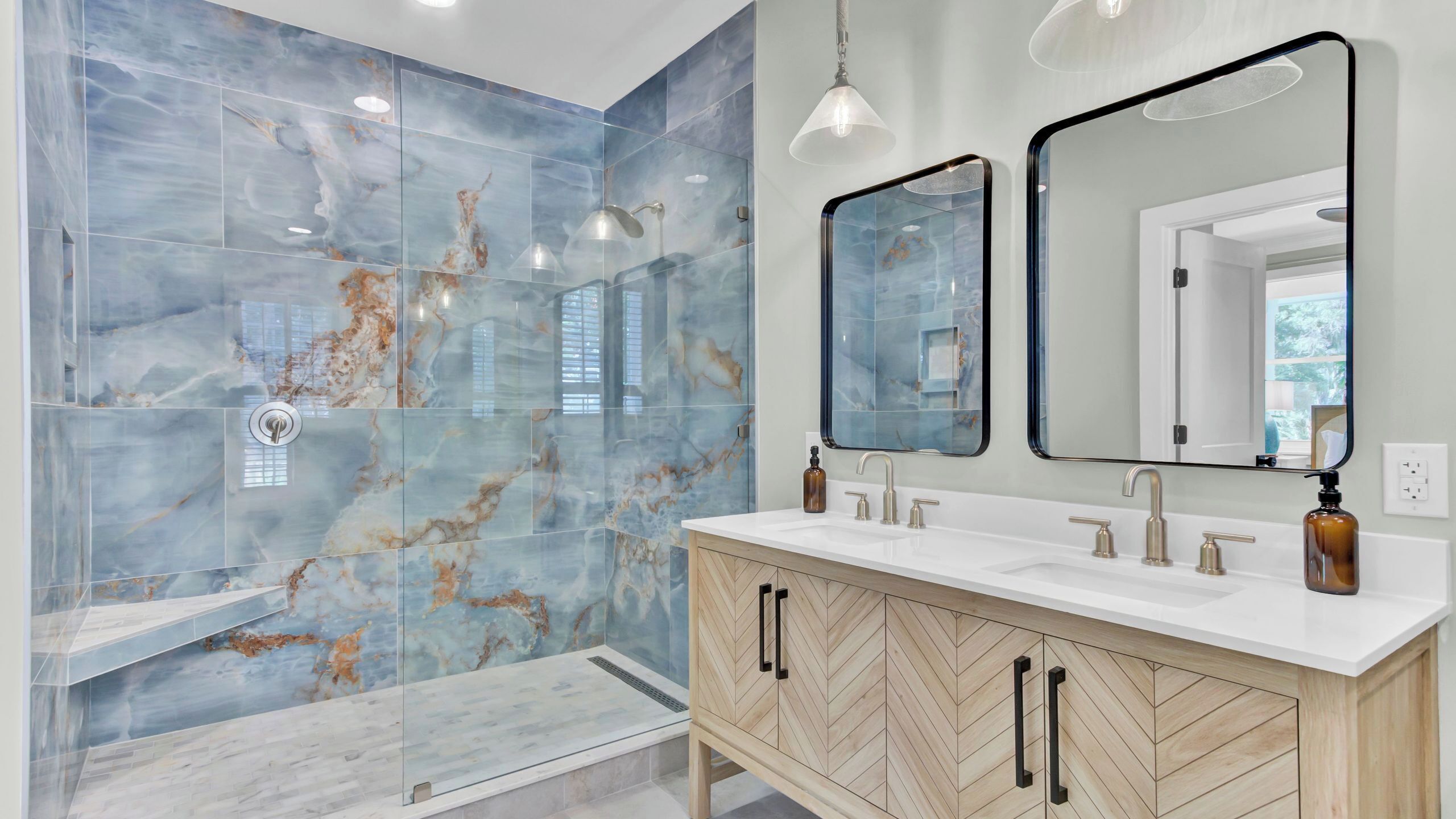 Une salle de bain moderne avec des carreaux de marbre, une douche à l’italienne, un meuble-lavabo double et des luminaires suspendus.