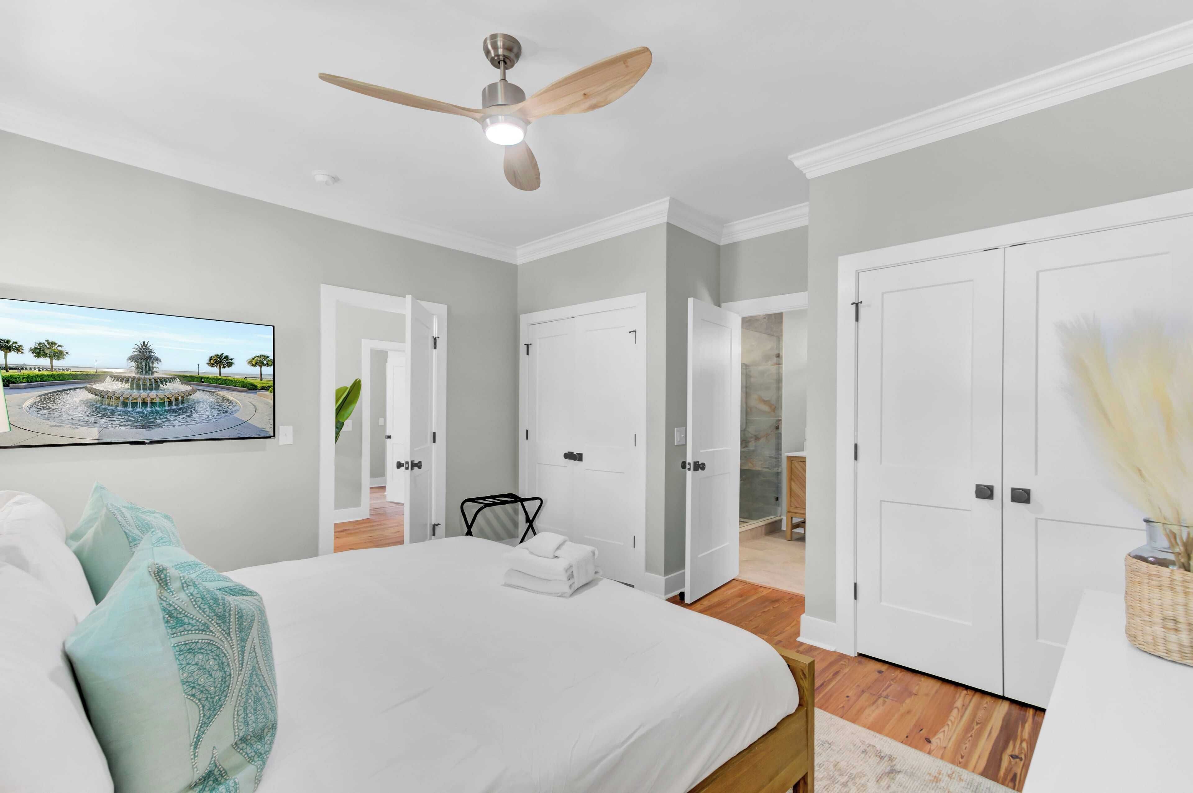 A bedroom with a large bed, a ceiling fan, and a TV displaying a landscape.