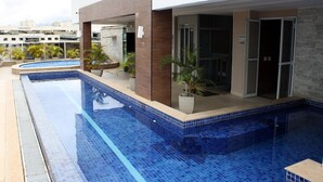 A swimming pool with a tiled edge, surrounded by a building with a modern design, including a stone wall and glass doors.