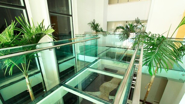 A modern indoor atrium with glass railings and multiple potted plants.
