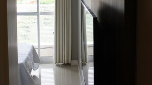 A room with a bed, a window with curtains, and a view of greenery outside.