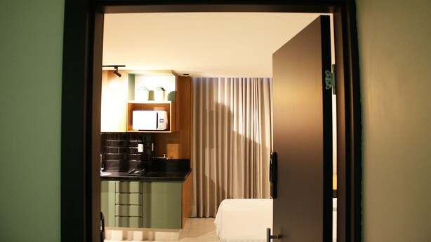 Une chambre d’hôtel avec une kitchenette, un lit et un rideau.