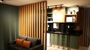 Un espace de vie compact comprenant un coin cuisine, un canapé avec des coussins et une cloison en bois.