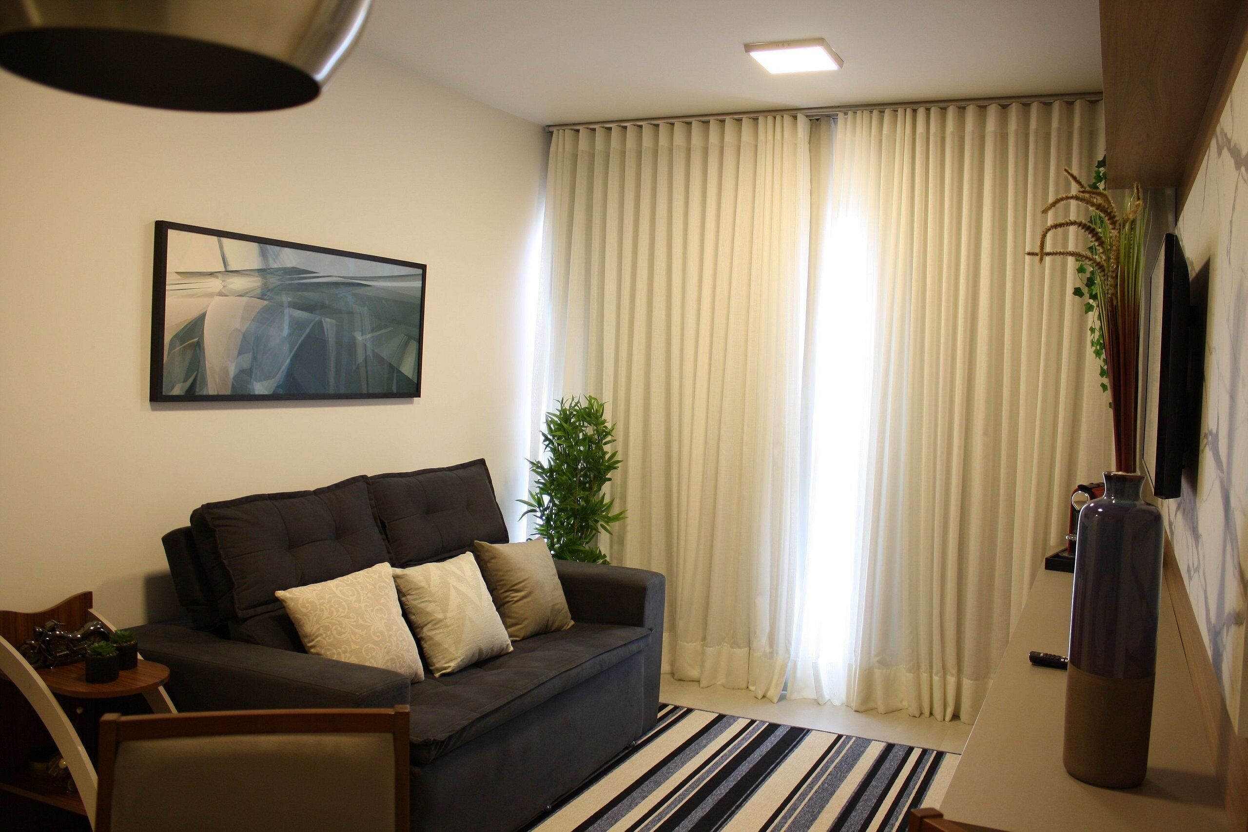 Una sala de estar con un sofá oscuro, una mesita, una planta en maceta y un cuadro en la pared.