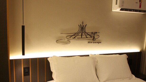 A neatly made bed with white linens, a wall-mounted air conditioner, and a pendant light fixture.