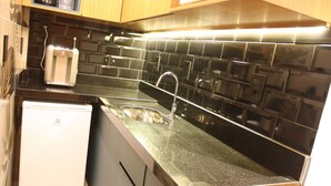 A kitchen with a black tiled backsplash, a stainless steel sink, and a white refrigerator.