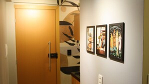 A hallway with a wooden door, a wall with abstract art, and three framed pictures.