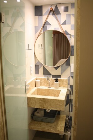 Une salle de bain dotée d’une douche à parois de verre, d’un lavabo avec un plan de travail en marbre, d’un miroir rond et d’un porte-serviettes.