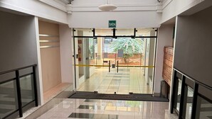 A clean, modern lobby with a glass entrance, a sign indicating the exit, and a tiled floor. - Flat Sudoeste Ed. Leonardo (Brasília)