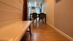 A hallway with a bench, two chairs, a table, and a painting on the wall. - Flat Sudoeste Ed. Leonardo (Brasília)