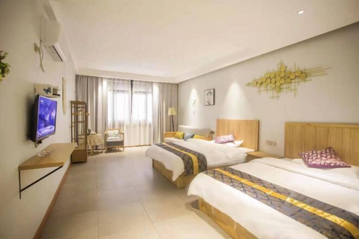 Habitación de hotel con dos camas, televisión, escritorio y ventana grande con cortinas.